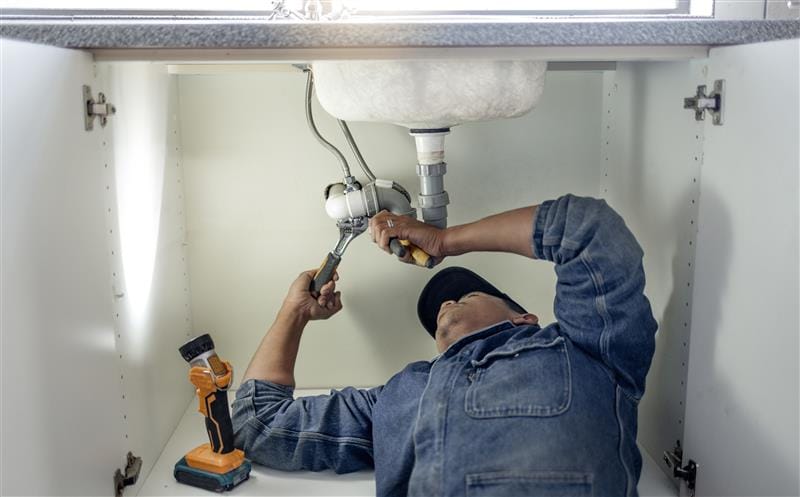 Plumber repairing pipes beneath a bathroom sink in New Castle