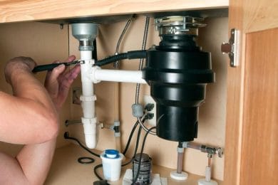 Plumber repairing a garbage disposal beneath a kitchen sink in New Castle