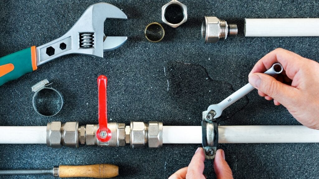 Plumber repairing a pipe valve with an adjustable wrench in New Castle