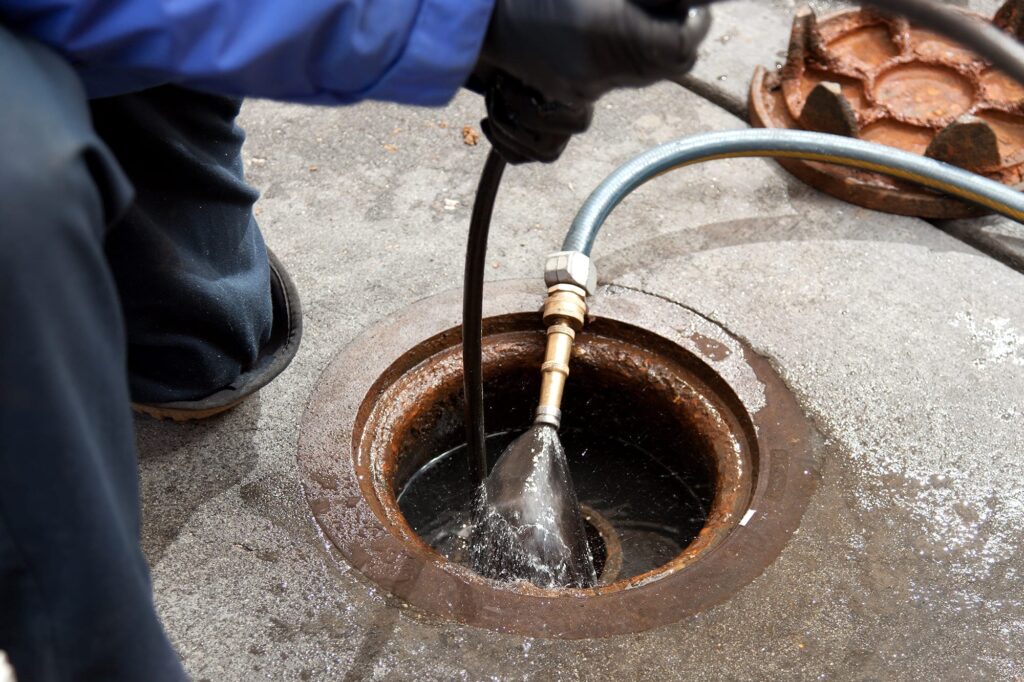 Plumber hydro jetting a sewer line through a manhole in New Castle