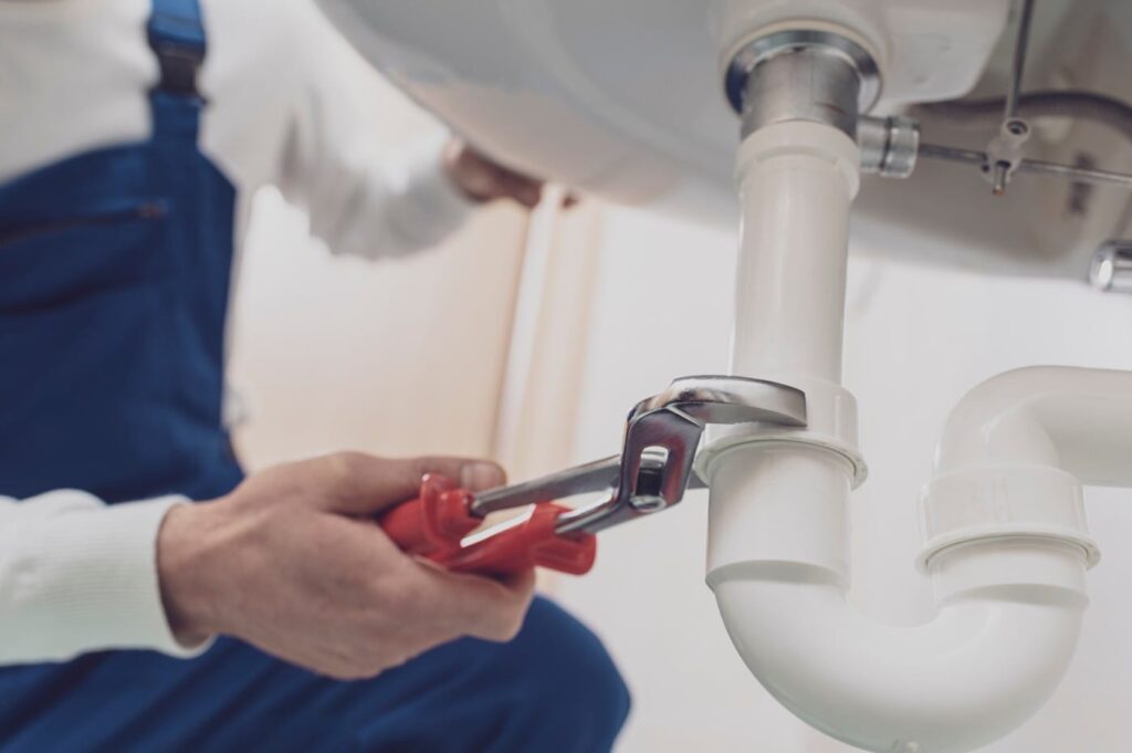 Plumber repairing a white drain pipe beneath a sink in New Castle