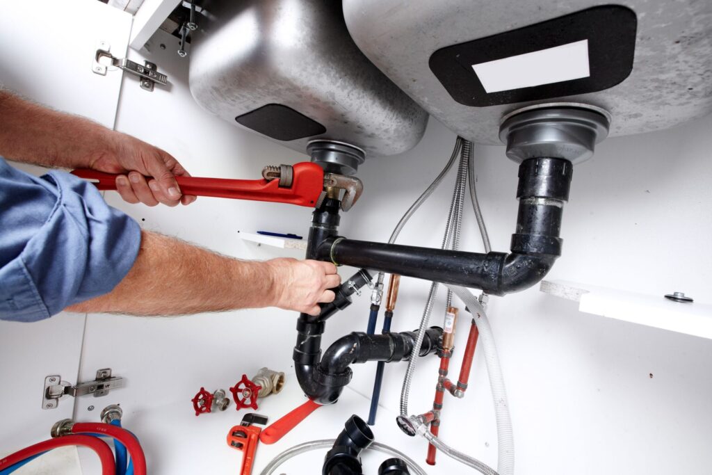 Plumber repairing drain pipes beneath a kitchen sink in New Castle