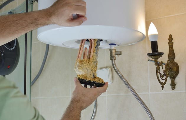 Technician removing mineral buildup from a water heater in New Castle